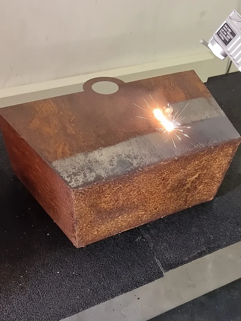 Laserreinigung entfernt Rost von einer Metalloberfläche, heller Laserpunkt und Funken sichtbar