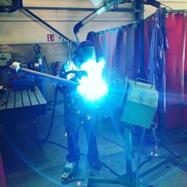 Ein Schweißer arbeitet mit einem Lichtbogen, um Metall zu verbinden, umgeben von Schweißschutz.