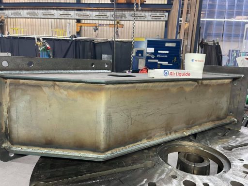 Schweißnaht an einem metallischen, rechteckigen Bauteil in einer Werkstatt.